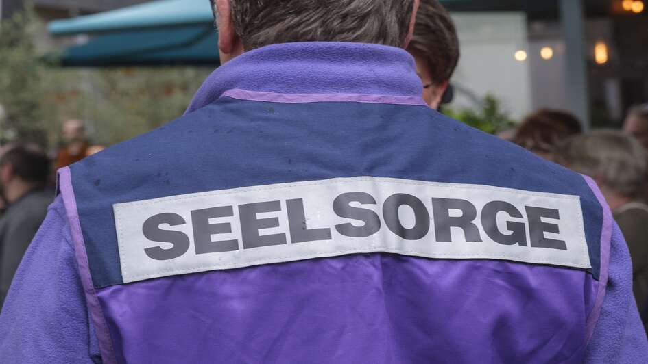 Es ist eine lila Jacke in der Rückenansicht zu sehen. Darauf die Aufschrift Seelsorge