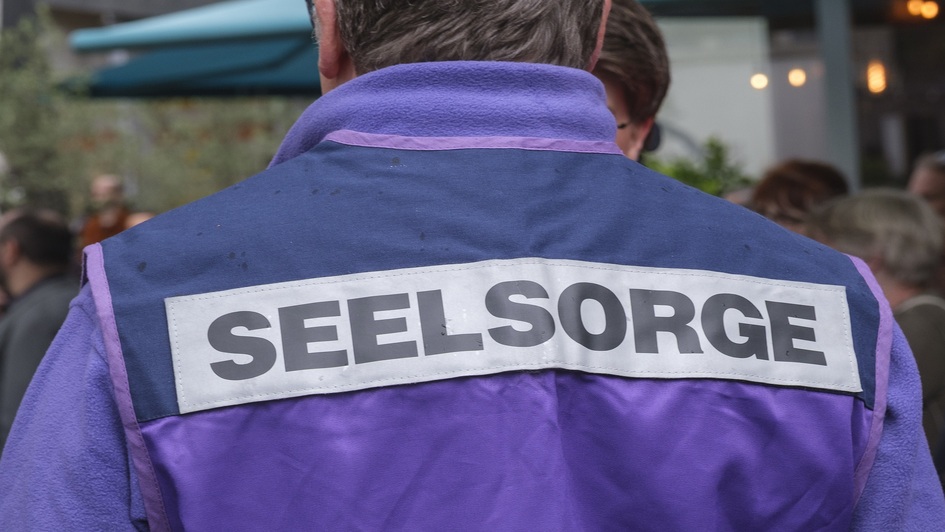Es ist eine lila Jacke in der Rückenansicht zu sehen. Darauf die Aufschrift Seelsorge