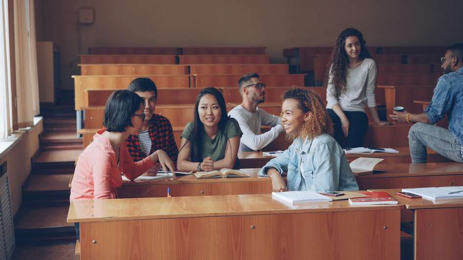 Ein Hoersaal in einer Universitaet. Mehrere stuierende sitzen auf den Stuehlen einander zugewanddt und unterhalten sich