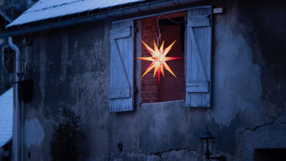 In einer offenen Türe einer Scheune hängt ein leuchtender Herrnhuter Stern