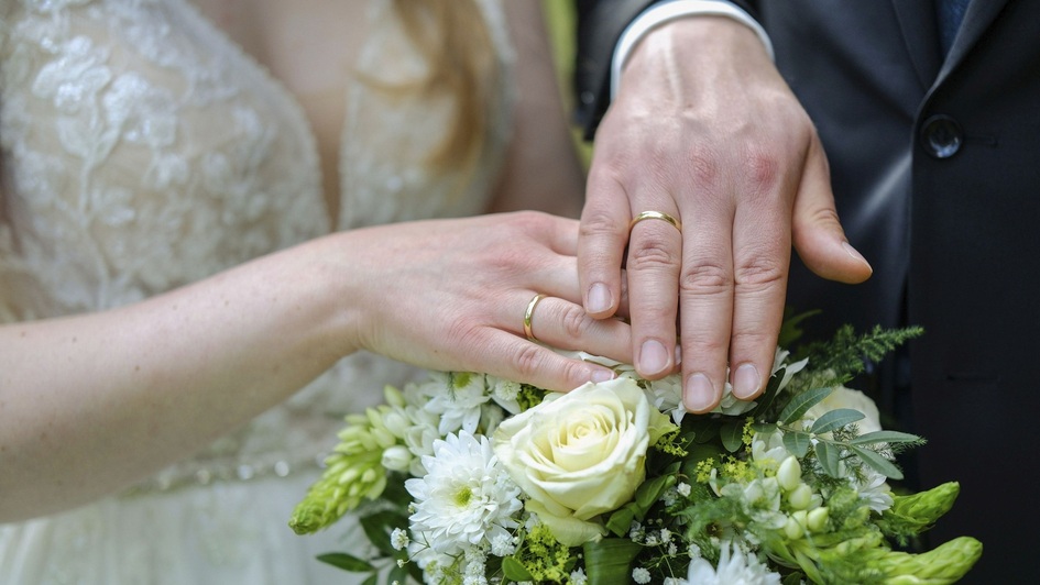 Hände eines Brautpaars mit Blumen und angestecktem Ring