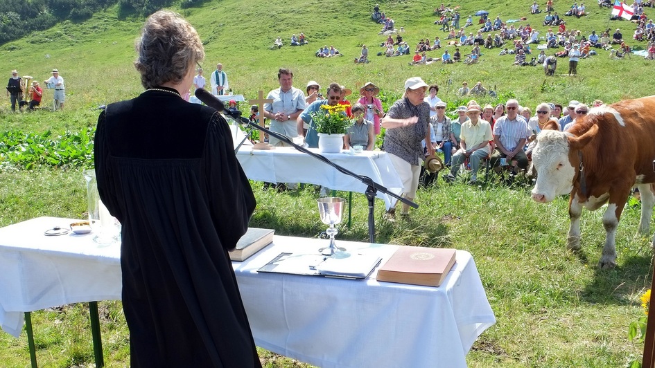 Pfarrerin  am Altar einen Bergottesdienst, im Hintergrund Besucher und Felsen