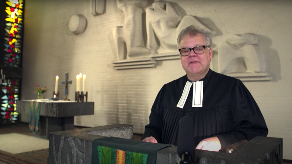 Pfarrer Carsten Krabbes auf der Kanzel. Er trägt ein lutherisches Bäffchen, im Hintergrund ist ein Kirchenfenster zu sehen.