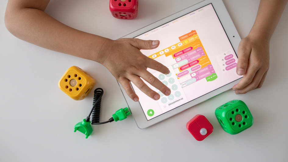 Kinderhände, die auf ein Tablet tippen. Daneben bunte Plastikwürfel. Kinderhände, die auf ein Tablet tippen. Daneben bunte Plastikwürfel.