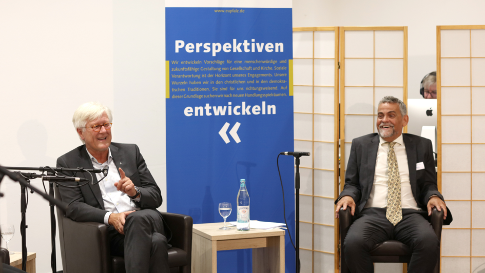 Zwei Männer (Heinrich Bedford-Strohm und Christoph Picker) sitzen in einem Tagungssetting vor einem Aufsteller mit der Aufschrift: 'Perspektiven entwickeln'. Zwei Männer (Heinrich Bedford-Strohm und Christoph Picker) sitzen in einem Tagungssetting vor einem Aufsteller mit der Aufschrift: 'Perspektiven entwickeln'.