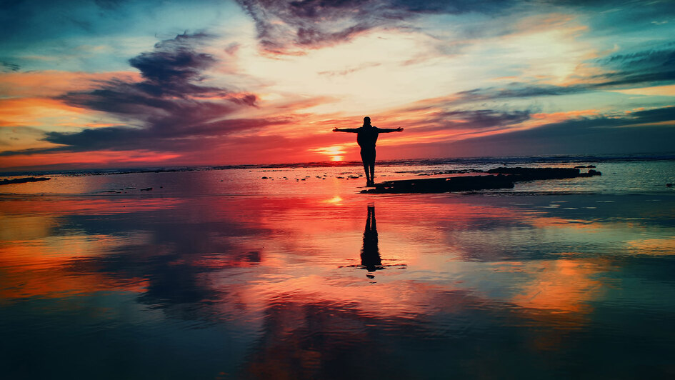FriedensBibel - Mann steht am Strand und breitet die Arme gen Sonnenuntergang aus FriedensBibel - Mann steht am Strand und breitet die Arme gen Sonnenuntergang aus