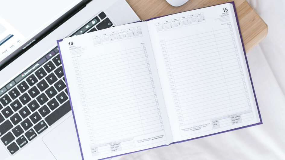 Ein Taschenkalender liegt quer über einem Laptop Ein Taschenkalender liegt quer über einem Laptop