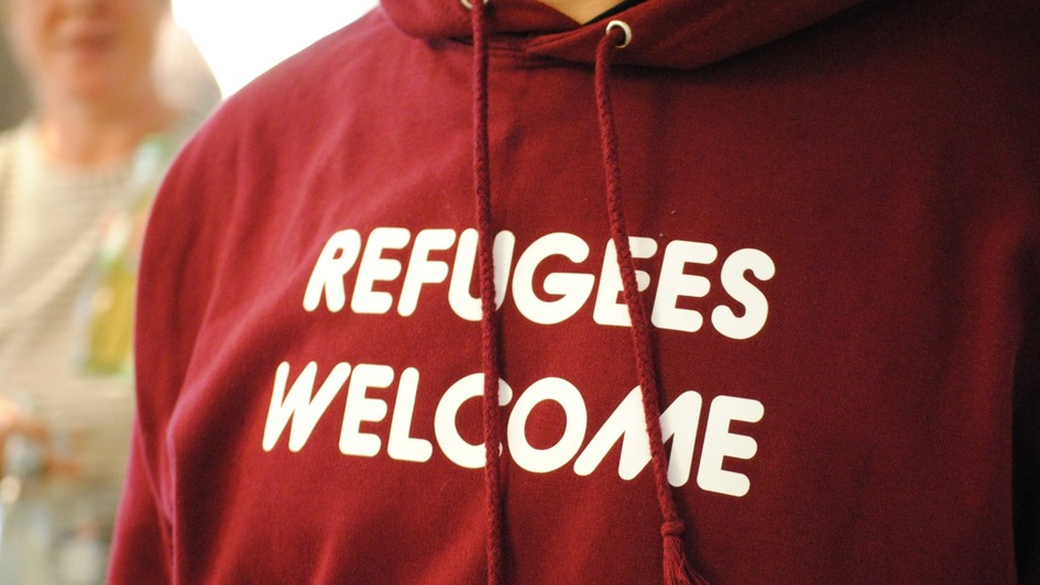 Symbolbild - Flucht und Integration: Eine Person trägt einen roten Kapuzenpulli, auf dem der Schriftzug 'Refugees Welcome' steht