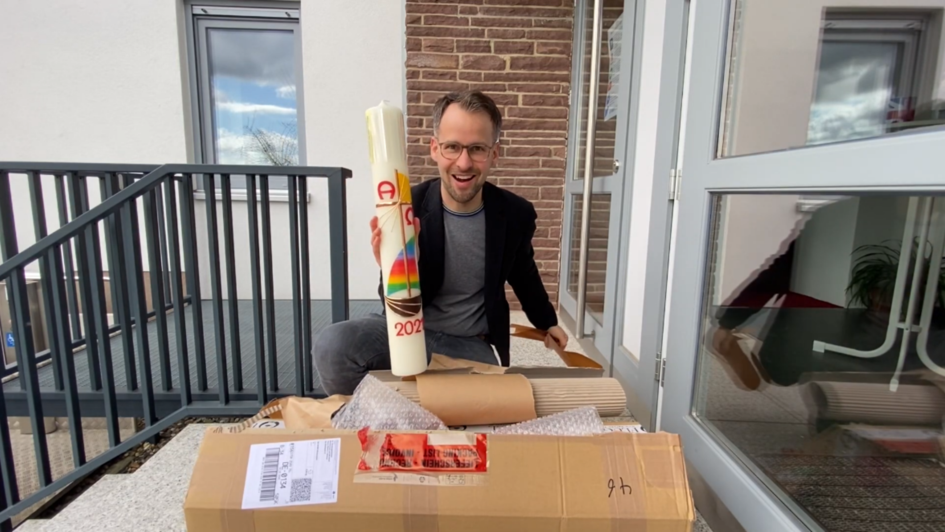 Pfarrer Johannes Böttner hält eine bunt verzierte Osterkerze in die Kamera.