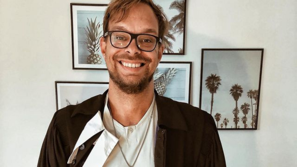 Pfarrer Nicolai Opifanti steht vor einer Wand, an der Bilder von Palmen hängen. Pfarrer Nicolai Opifanti steht vor einer Wand, an der Bilder von Palmen hängen.