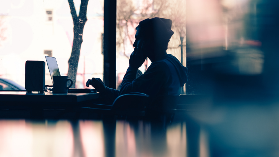 Siluette von einem Menschen an einem Tisch mit Laptop Kaffebecher vor einem großen Fenster. Siluette von einem Menschen an einem Tisch mit Laptop Kaffebecher vor einem großen Fenster.