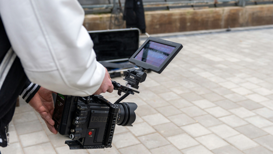 Eine Person in weißer Jacke hält eine professionelle RED-Kamera mit externem Monitor, bereit für eine mobile Videoaufnahme.