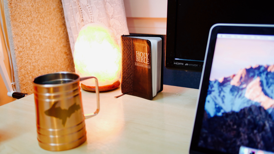 Schreibtisch mit Laptop, Salzkristalllampe, Trinkgefäß und Bibel