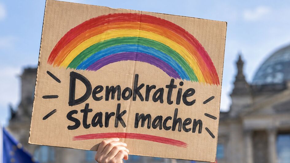 Hochgehaltenes Protestschild mit Regenbogen und der Aufschrift ‚Demokratie stark machen.