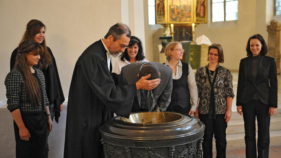 Ein Pfarrer tauft einen jungen Erwachsenen