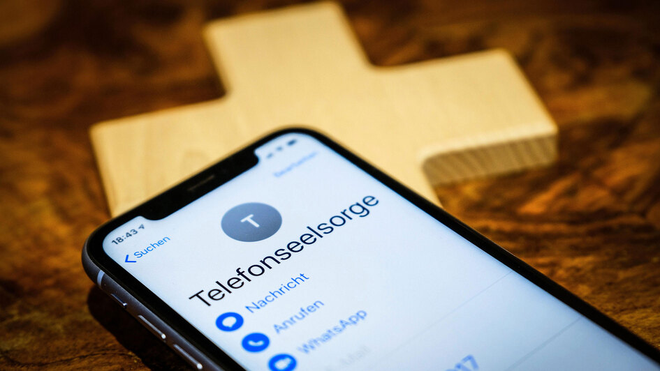Handy mit der Anzeige Telefonseelsorge auf einem kleinen Holzkreuz
