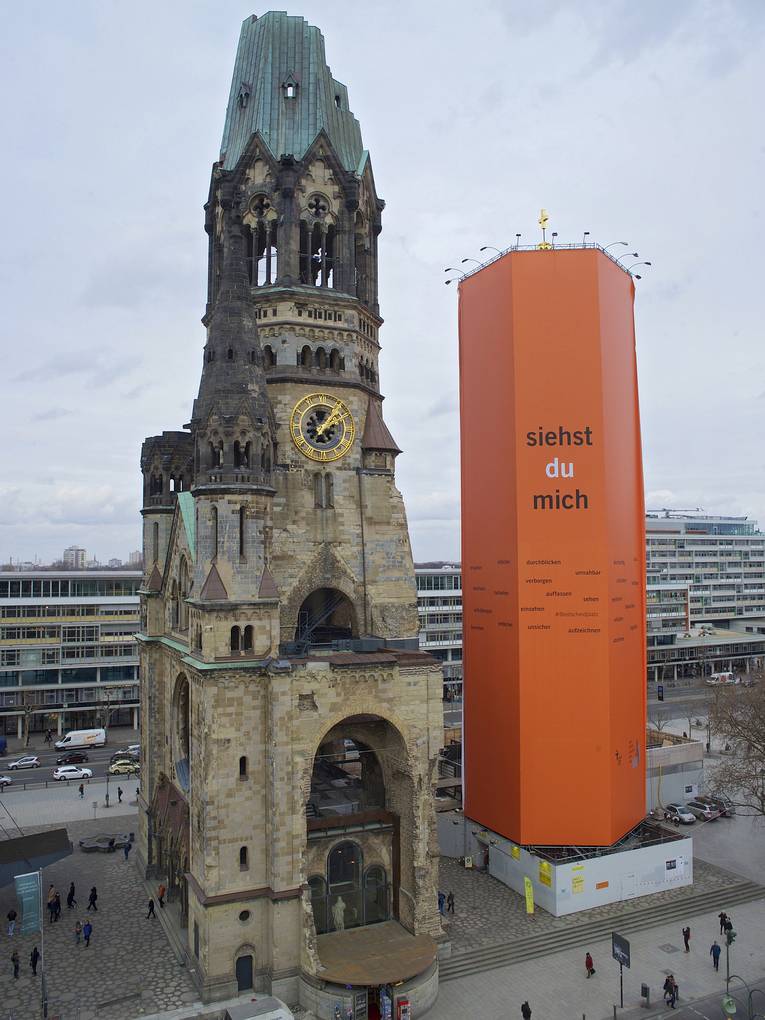 Die Türme der Kaiser-Wilhelm-Gedächtniskirche mit Orangem Fassadenplakat zum Evangelischen Kirchentag 2017