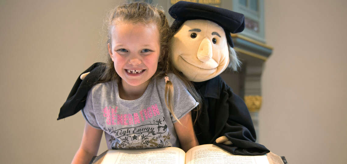 Mädchen und Handpuppe Martin Luther sitzen über einer Bibel