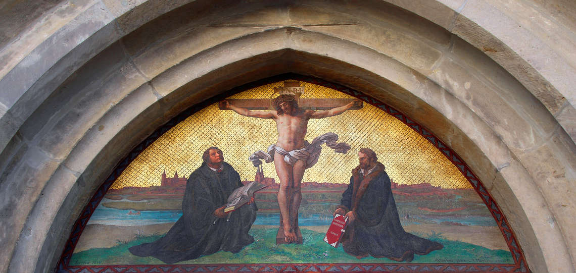 Darstellung des gekreuzigten Jesus mit den Reformatoren Martin Luther (1483-1546, li.) und Philipp Melanchthon (1497-1560) über der "Thesentür" der Wittenberger Schlosskirche.