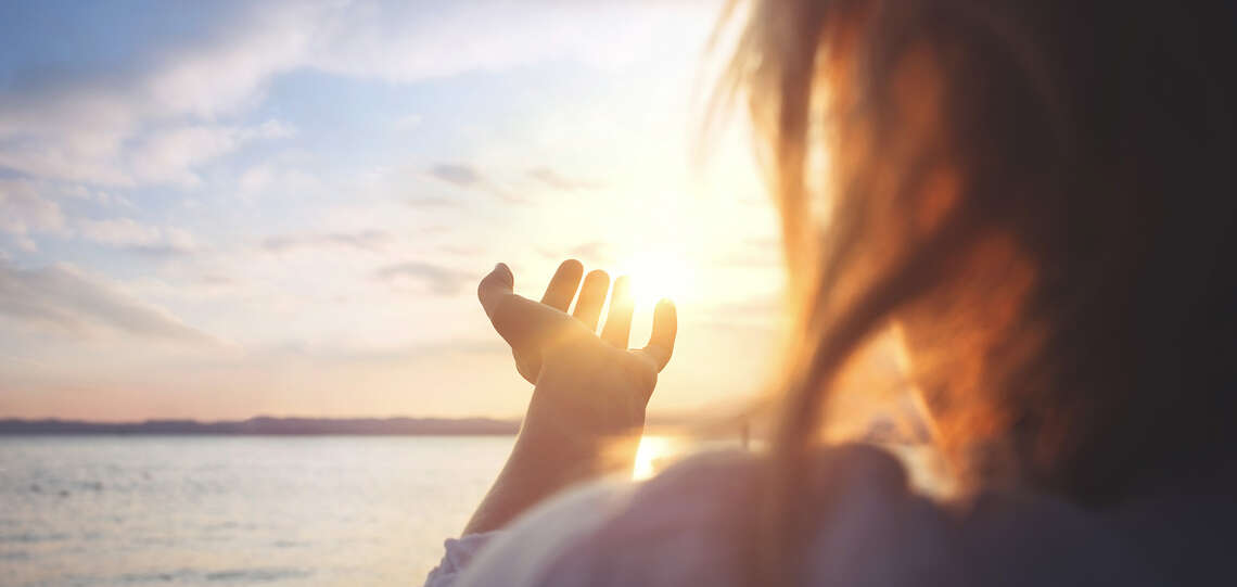 Eine Frau betrachtet einen Sonnenaufgang über einem Gewässer.