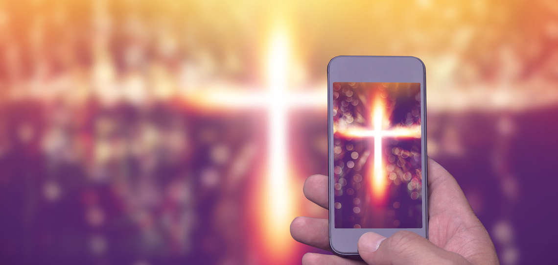Mann macht mit seinem Smartphone ein Foto von einem Kreuz