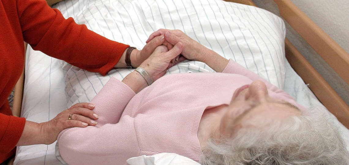Eine ehrenamtliche Sterbebegleiterin sitzt am Bett einer kranken Pflegeheimbewohnerin.