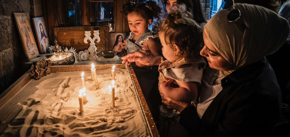In einer Kirche in Homs, Syrien: Eine Frau (Christin) zeigt ihrer Freundin (Muslimin) diese Kirche, gemeinsam mit ihren Kindern zünden sie Kerzen an.