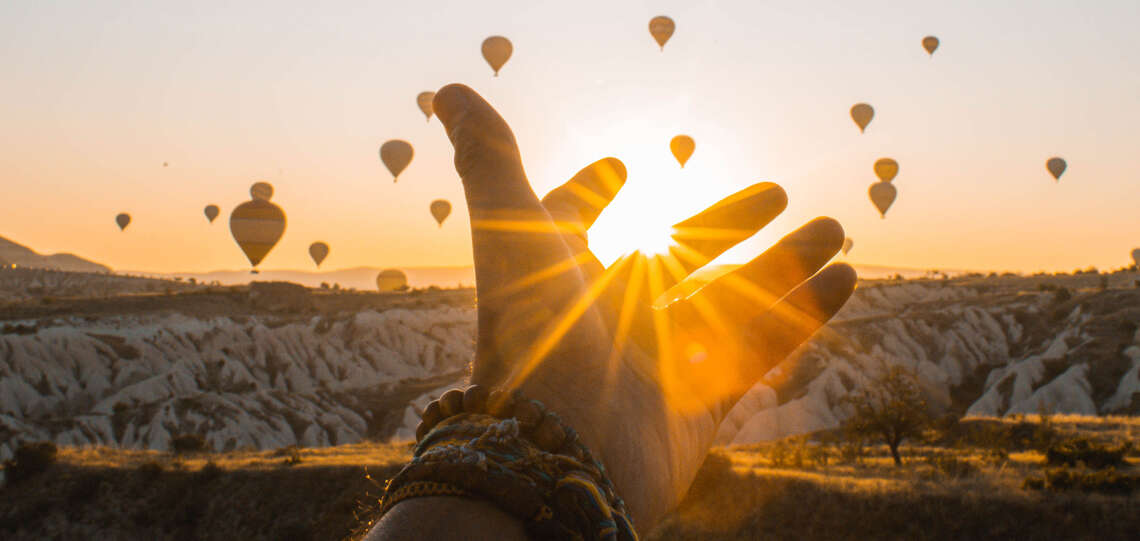Hand im Sonnenaufgang und Heißluftballons im Hintergrund Hand im Sonnenaufgang und Heißluftballons im Hintergrund