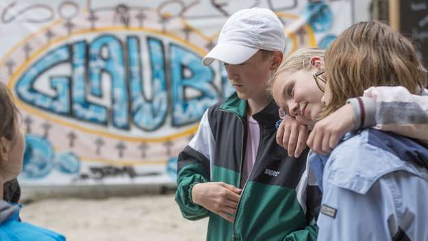 Drei Jugendliche umarmen sich vor einem Graffity-Plakat