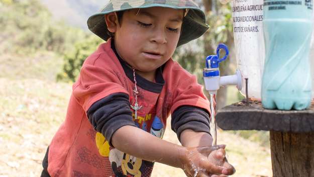 Junge wäscht sich seine Hände mit Wasser aus einem Kanister