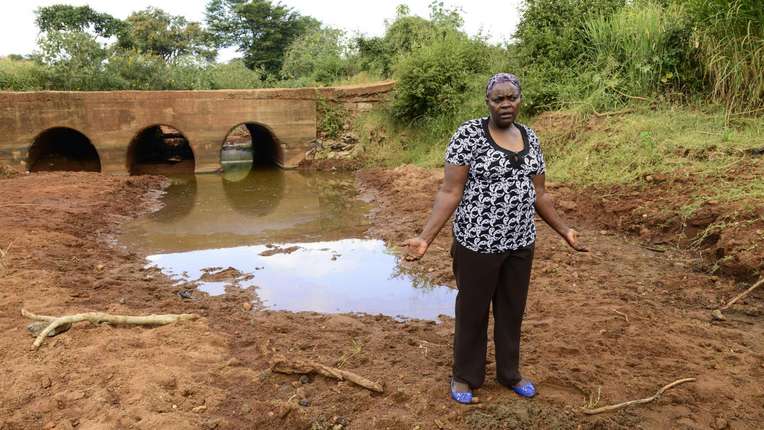 Frau in Kenia vor einer schlammigen Wasserstelle