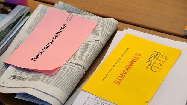 Unterlagen, Tageszeitung und Stimmkarte auf dem Tisch eines Synodalen