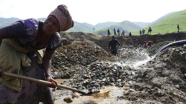 Eine Minenarbeiterin Minenarbeiter in Fungamwaka (Demokratische Republik Kongo) trennt im Wasser, das in die Mine geleitet wird, mit einer Schaufel grobes Gestein von Sand und Schlamm.