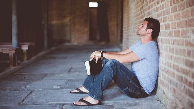 Mann sitzt mit einer Bibel auf dem Boden einer Kirche