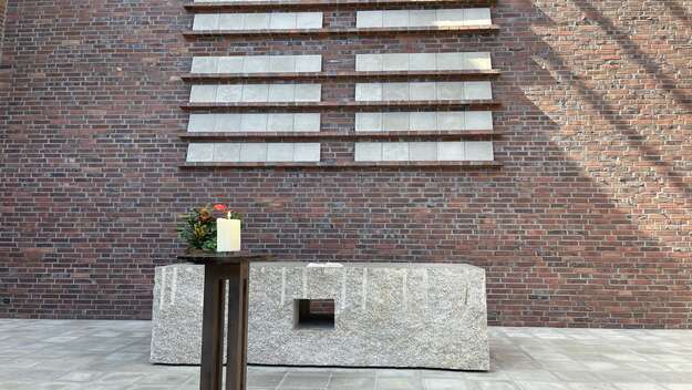 Zu sehen ist der Altar der Autobahnkirche Medenbach. Dieser besteht aus einem massiven Granitblock. Er ist nicht geschmueckt. Lediglich eine Bibel liegt aufgeschlagen darauf sowie ein florales Gesteck steht an der Seite. 