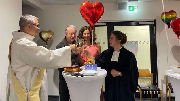 Diakon Gerorg Fischer links im Bild und Pfarrerin Mirjam Biskamp-Krämer rechts im Bild. In der Mitte hinter dem Stehtisch steht das Brautpaar. Alle vier Stoßen mit Sekt an. 