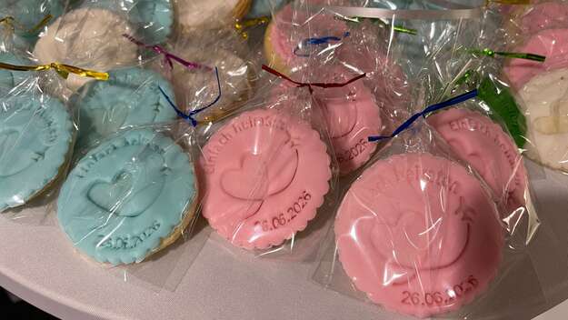 Selbstgebackene verzierte große Kekse, eingepackt in durchsichtige Tütchen. Die Kekse sind mit rosa oder hellblauem Zuckerguss und der Aufschrift einfach heiraten, einem Herz und Flugzeug verziert. 