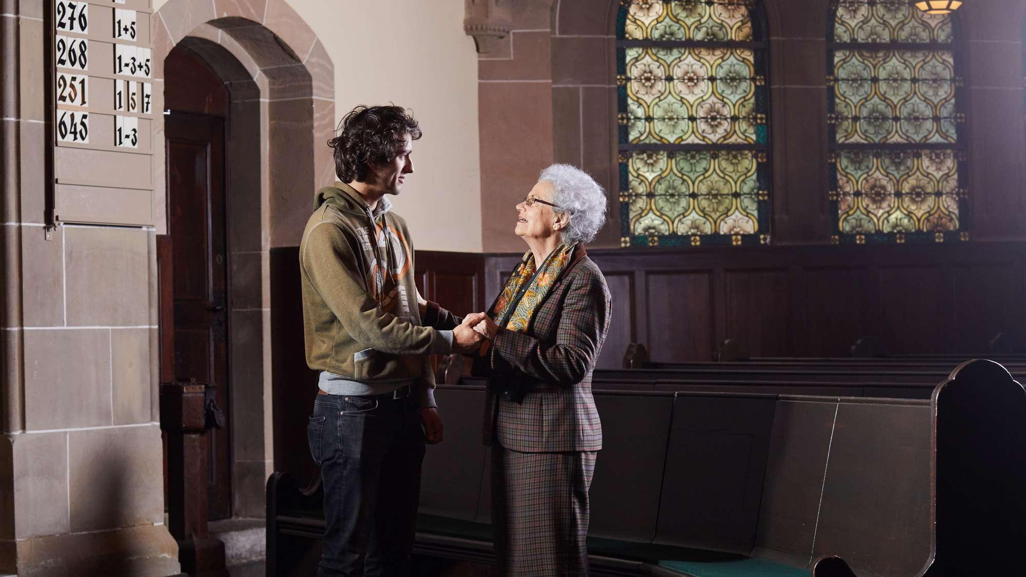 Ein junger Mann steht mit einer älteren Frau in einer Kirche und hält ihre Hand.