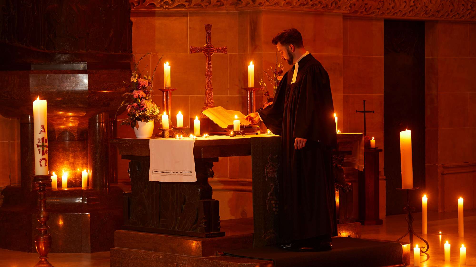 Ein Pfarrer steht in einer von Kerzen erleuchteten Kirche am Altar.