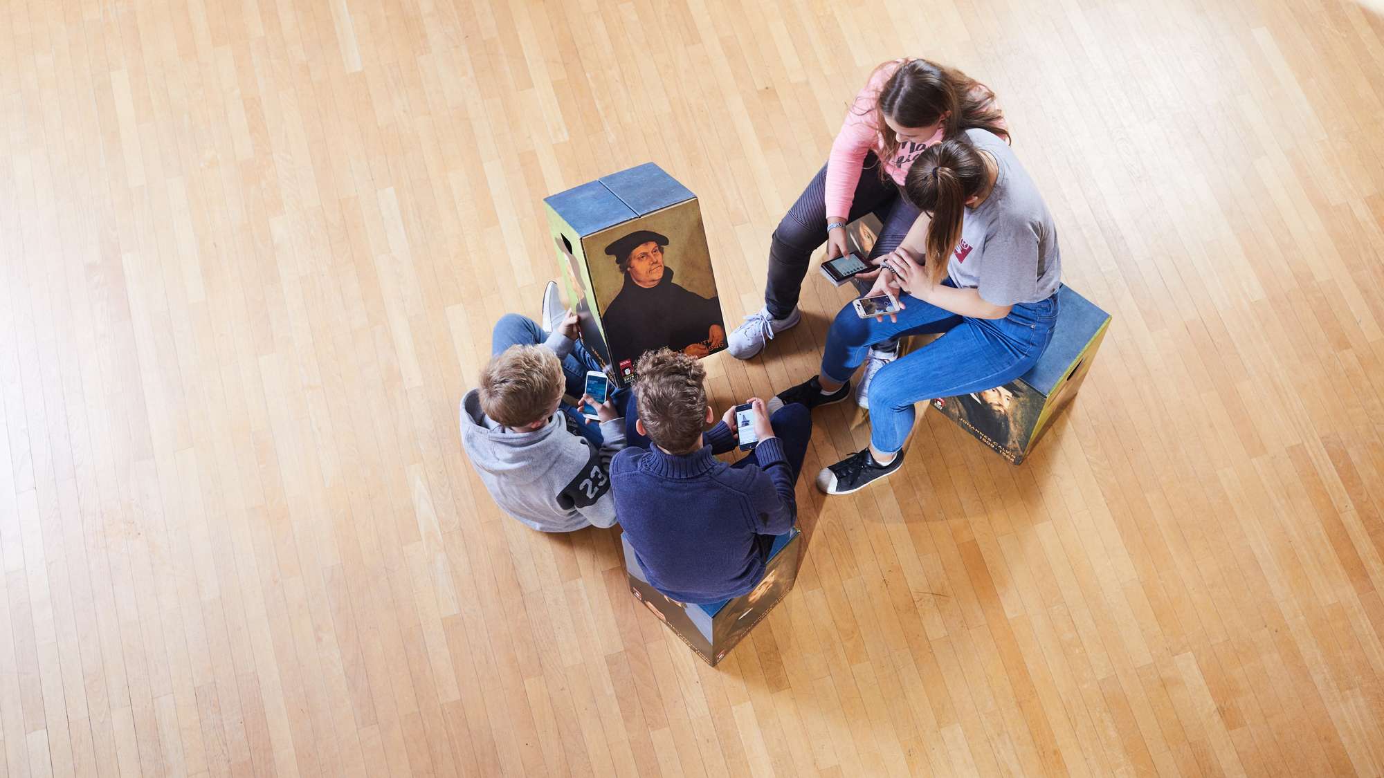 Vier Jugendliche betrachten ein Porträt Martin Luthers auf einem Hocker.