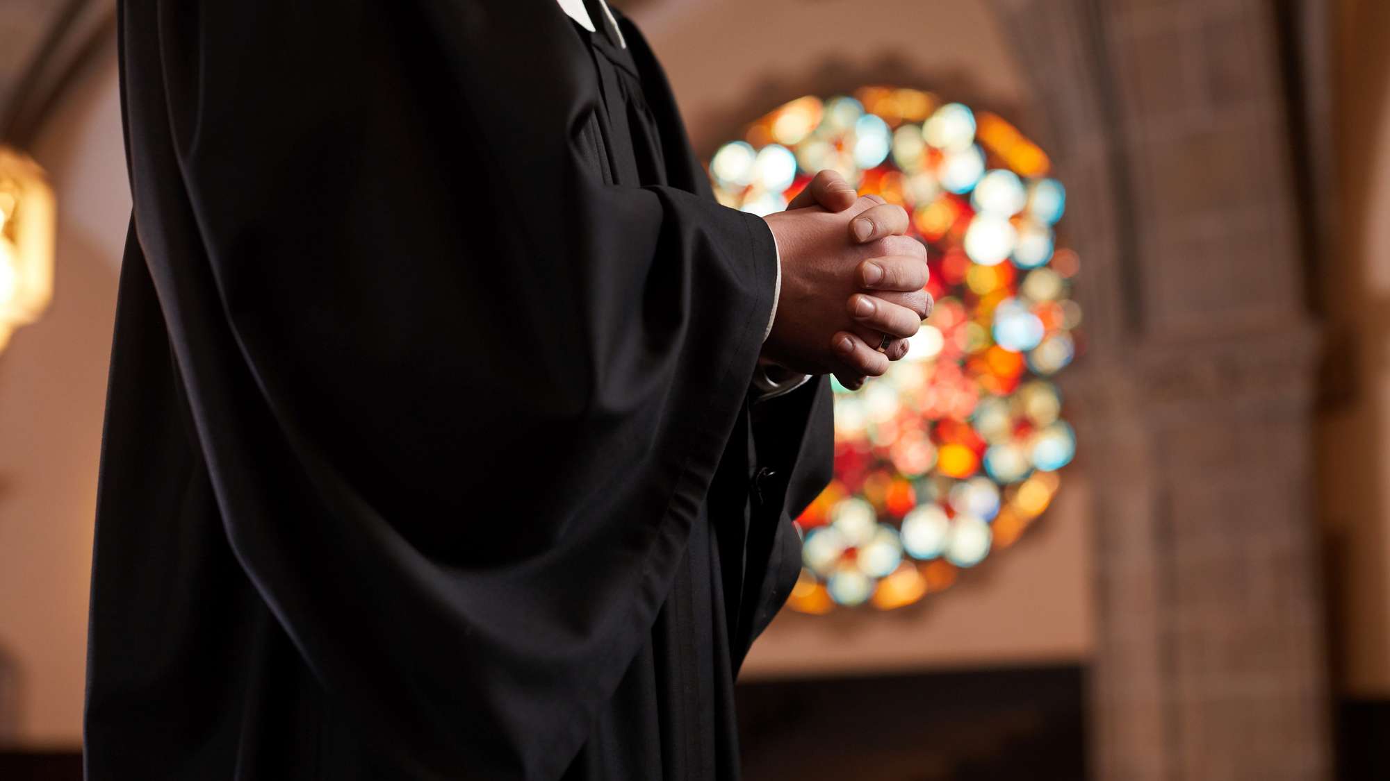 Pfarrer betet mit gefalteten Händen in einer Kirche.