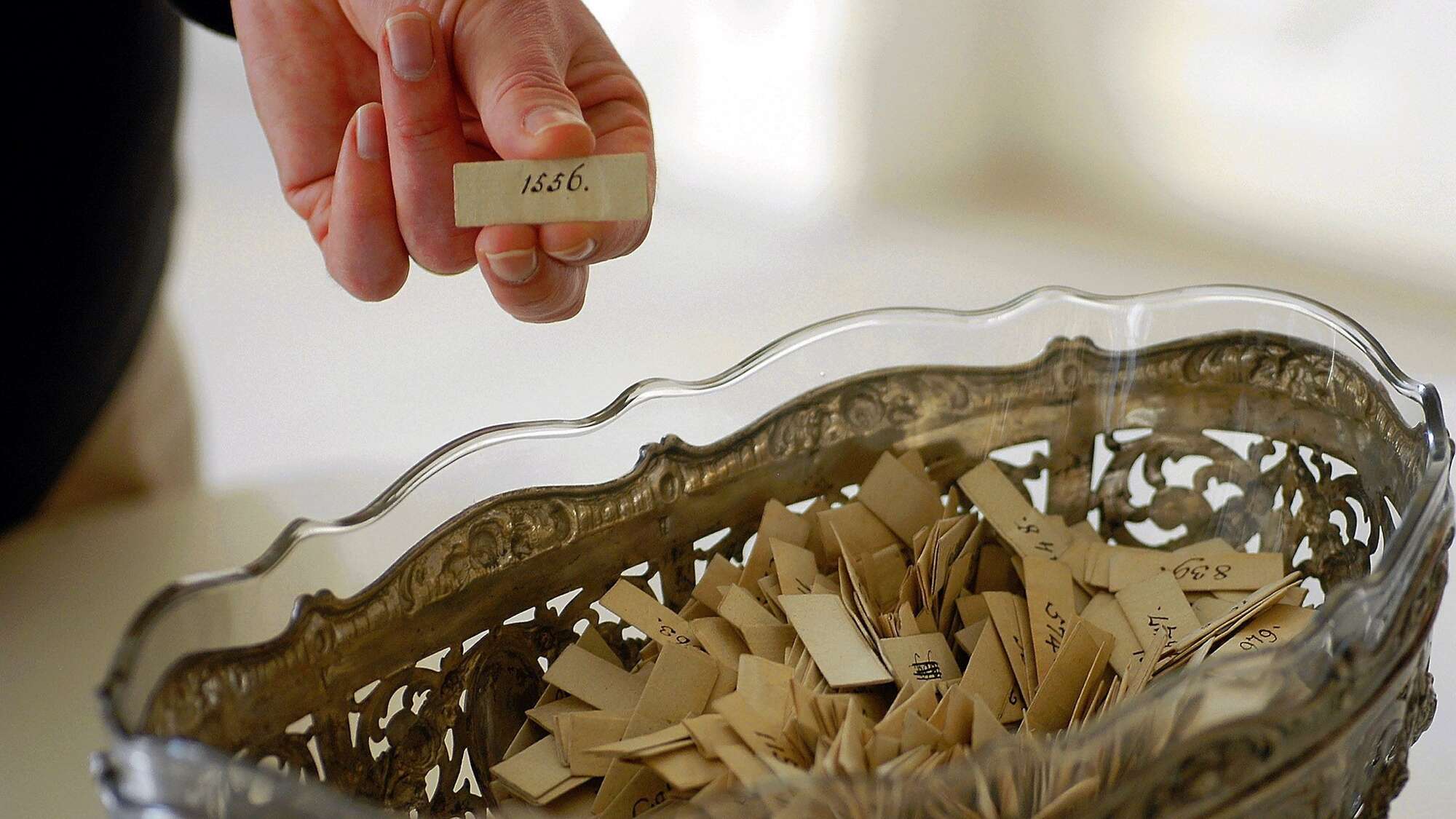 Hand zieht eine Tageslosung aus einer Schale mit Losnummern