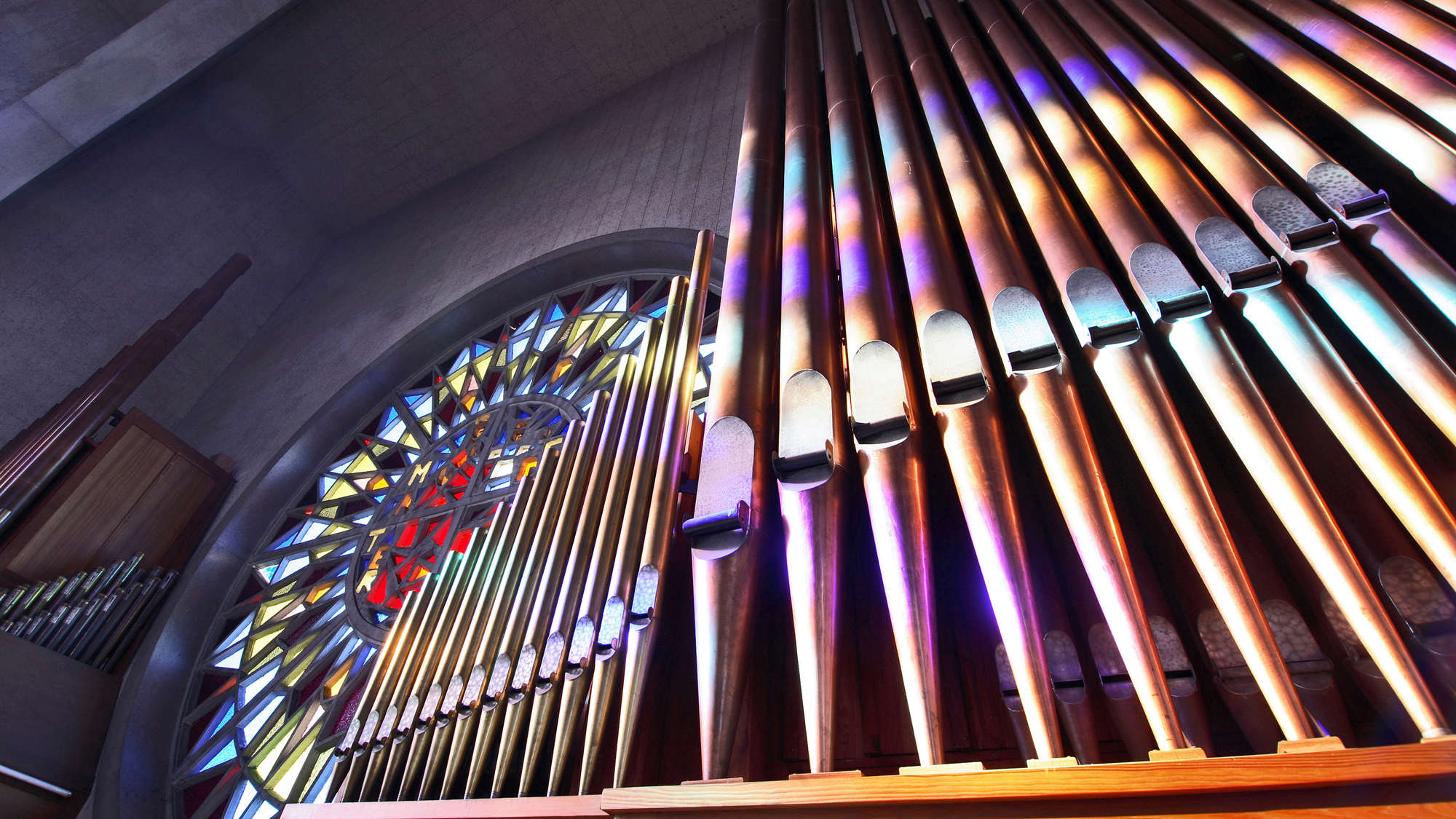Orgelpfeifen neben einem Buntglasfenster in einer Kirche.