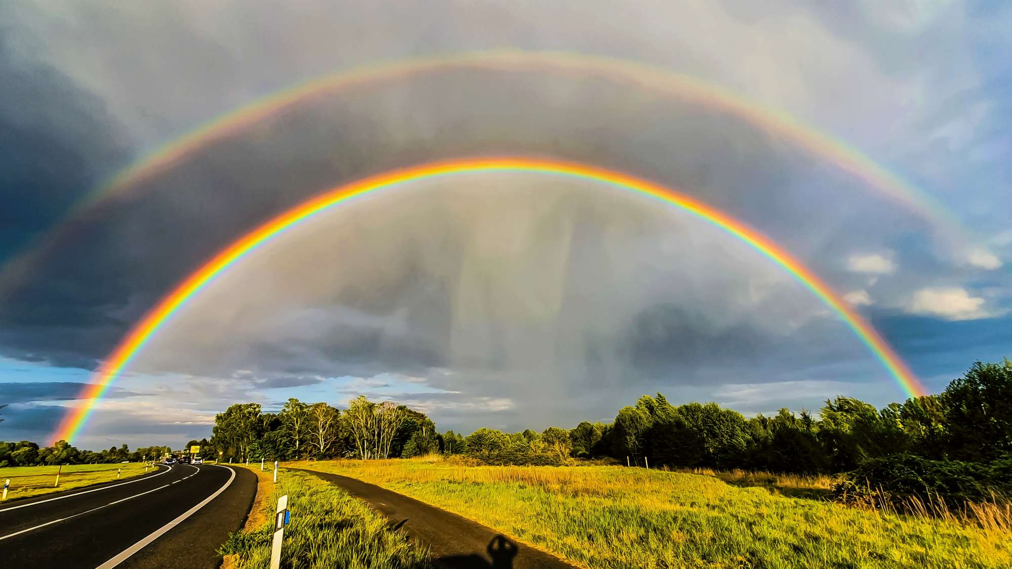 Ein doppelter Regenbogen über einer Landstraße und Natur.