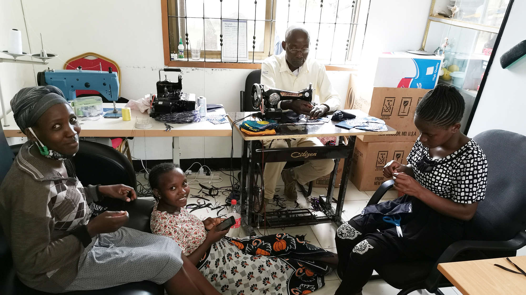 Titelbild Momente der Ökumene: Eine schwarze Familie näht in ihrem Wohnzimmer Stoddmassken