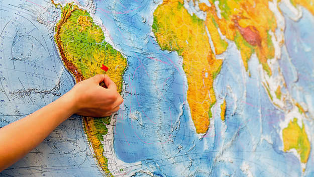 Hand with a pin in front of a world map.
